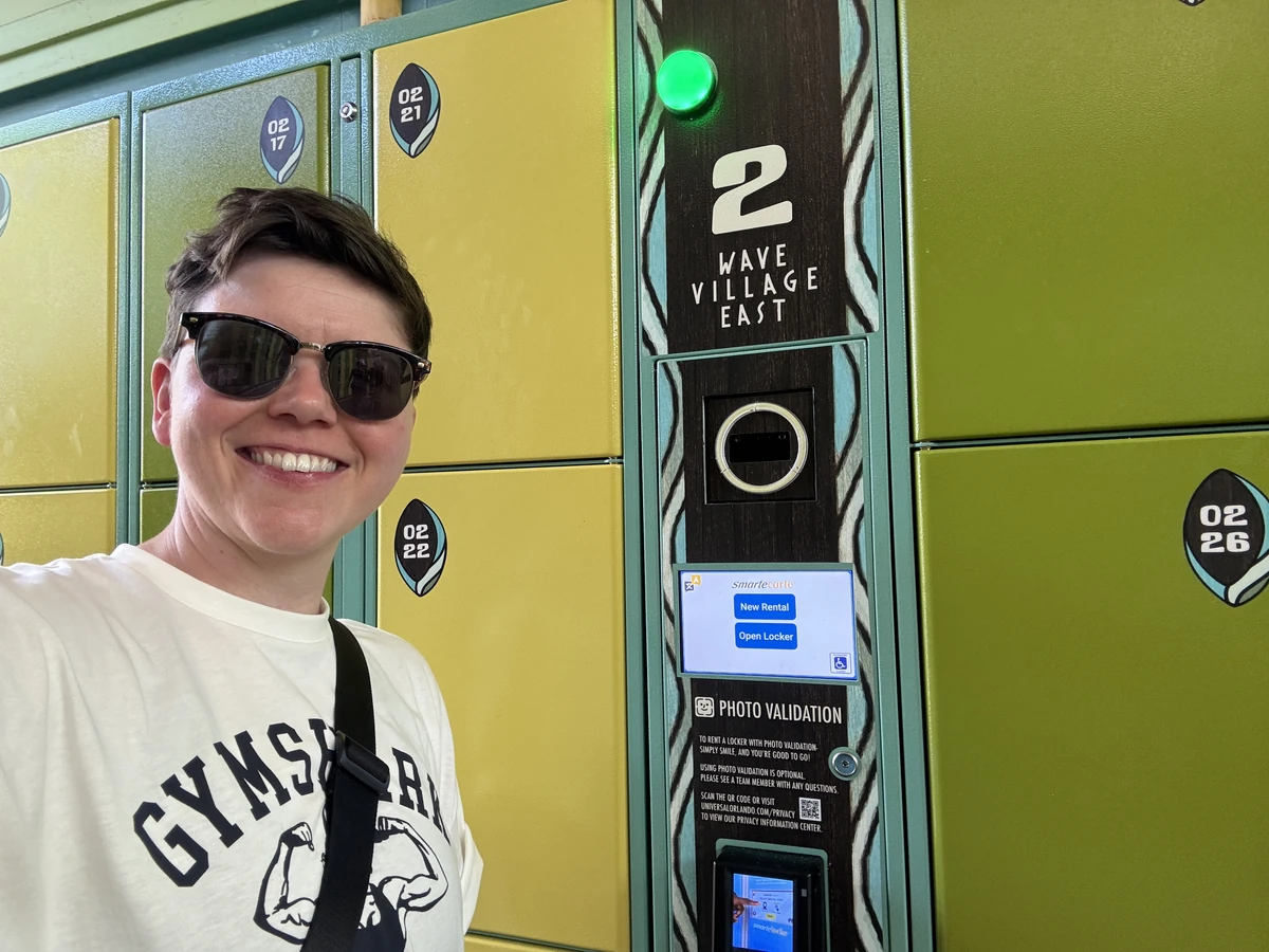 Cora next to Wave Village East locker station 2 at Volcano Bay water park, with the green availability light visible