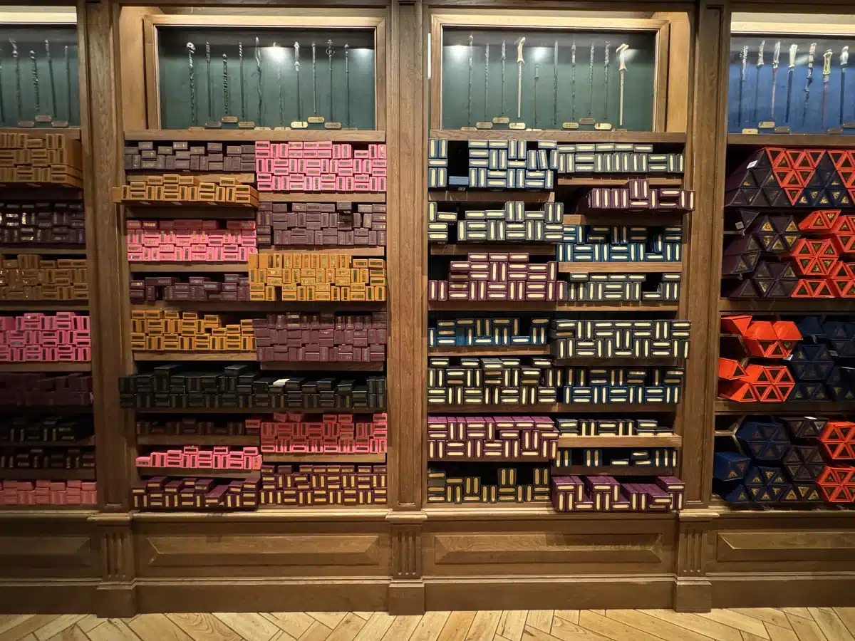 Cosme Acajor Baguettes Magique colourful wand boxes on wooden shelves at Place Cachée Wizarding World of Harry Potter Epic Universe.